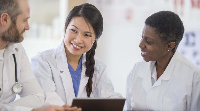 A medical resident speaks to two of her colleagues while holding a medical chart.