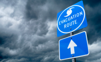 When Disaster Strikes: How to Maintain Continuity of Care. An Evacuation Route sign in the foreground with the clouds of an incoming hurricane in the background.