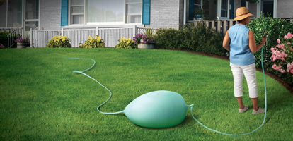 A woman watering flowers with her garden hose and ignoring the clogged and expanding hose behind her.