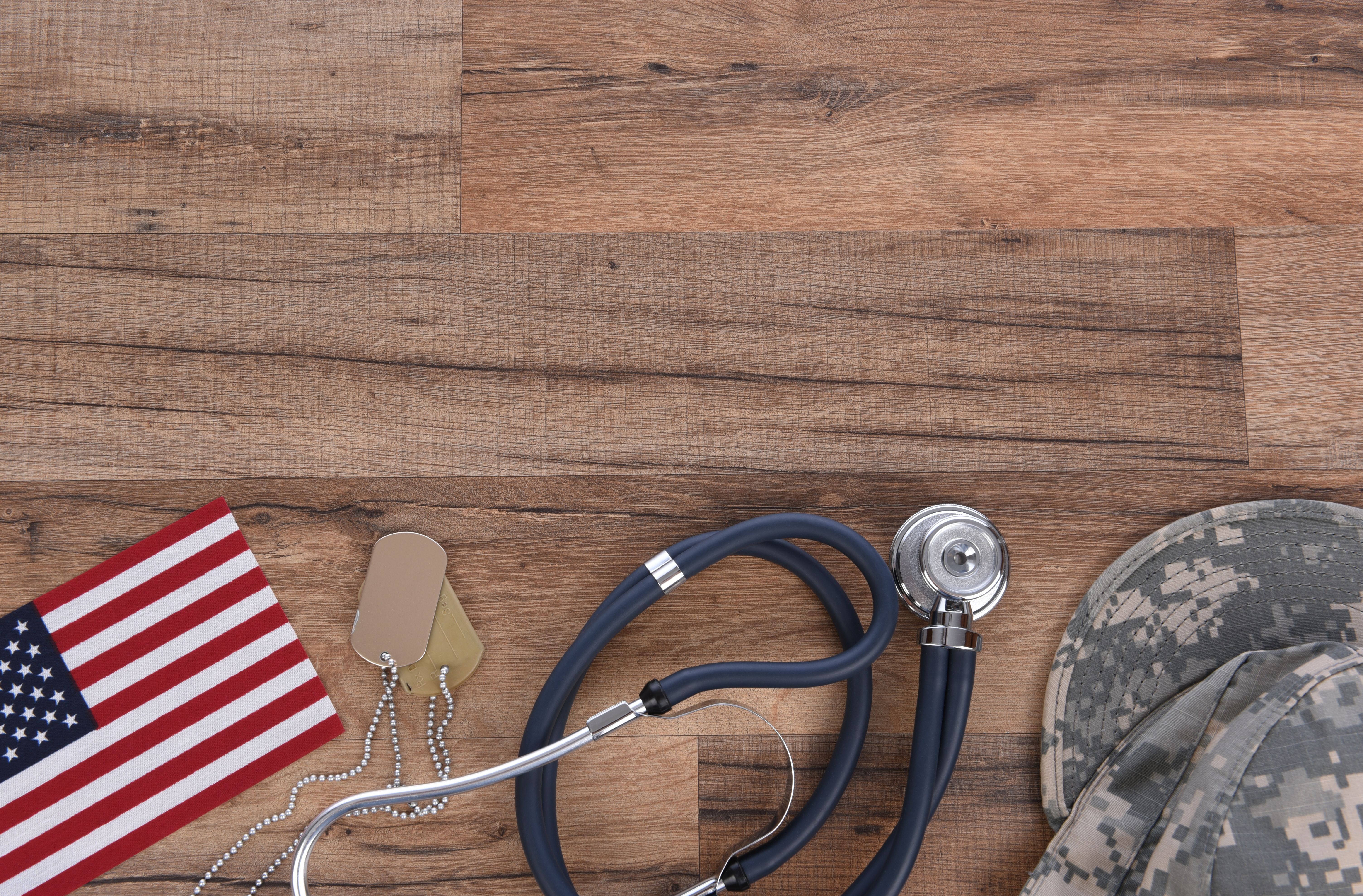 Military and Veterans Health Care Concept. Dog tags, American Flag, military camo hat and stethoscope on a wood background - Steve Cukrov - adobe.stock.com