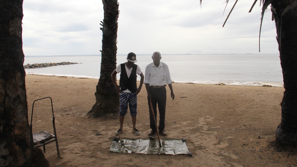 
Engeye Nbondwange gives a geography lesson to motorcycle taxi driver Ferdinand on the beach at Banana Point [William Clowes/Al Jazeera]
