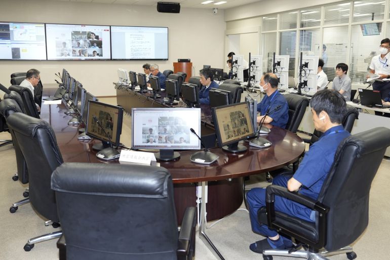 People sitting around a table at Japan's meteorological agency, There are large screens on the wall behind them and at the desks.