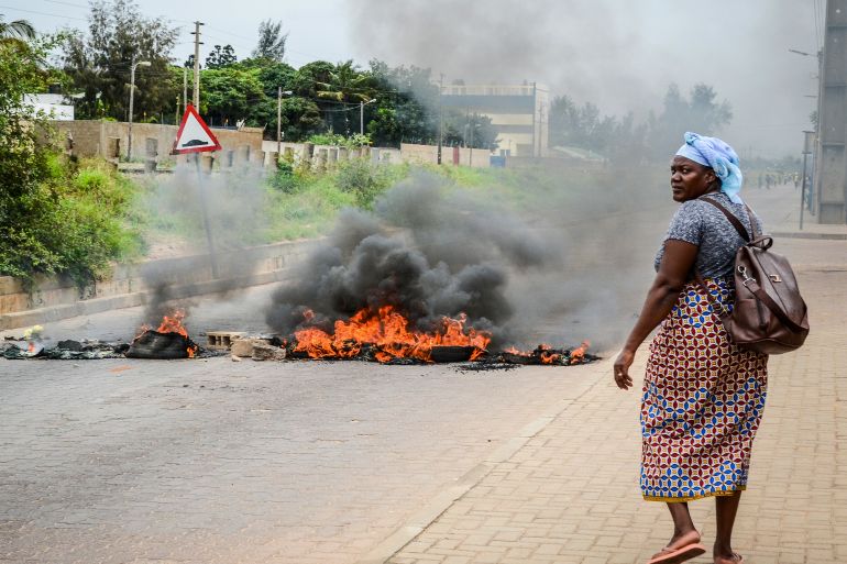 A woman walks past a barricade set fire by protesters in Maputo, Mozambique, Thursday, Nov. 7, 2024. Protesters dispute the outcome of the Oct. 9 elections that saw the ruling Frelimo party extend its 49-year rule. (AP Photo/Carlos Uqueio)