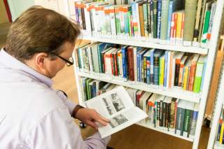 Ein Mensch hockt vor einem Bücherregal. In seinen Händen hält er ein aufgeschlagenes Buch