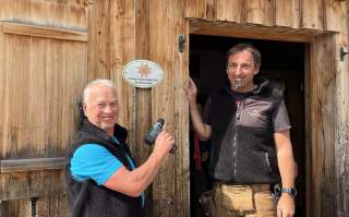 Zwei Personen bringen das Siegel an Hüttenwand an