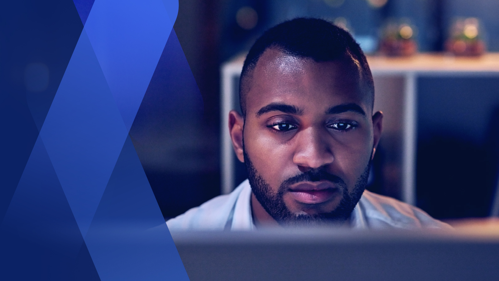 Businessman in business casual attire in dark office working on laptop, tight frame