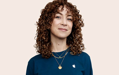 カメラの方を見ているカーリーヘアのApple Retailのスタッフ。