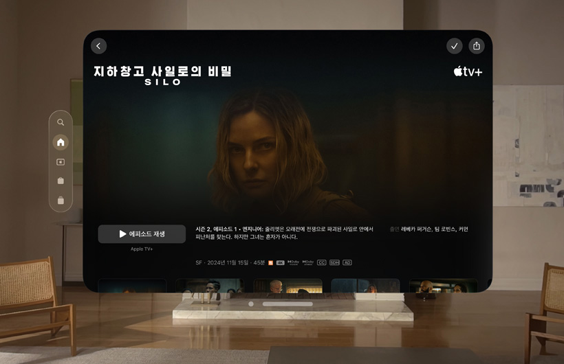 Apple Vision Pro로 경험하는 Apple TV 화면이 거실에 떠 있는 모습. Apple TV+ 시리즈 '지하창고 사일로의 비밀' - Silo의 정지 이미지가 보입니다.