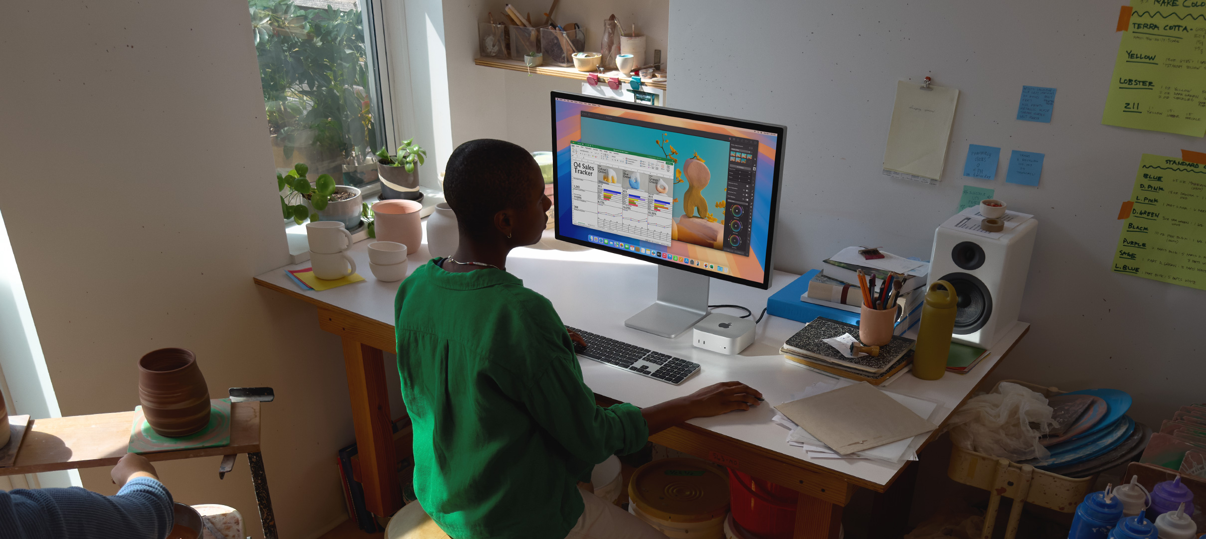 A person uses Mac mini at a desk, viewing a display screen with colour app activity