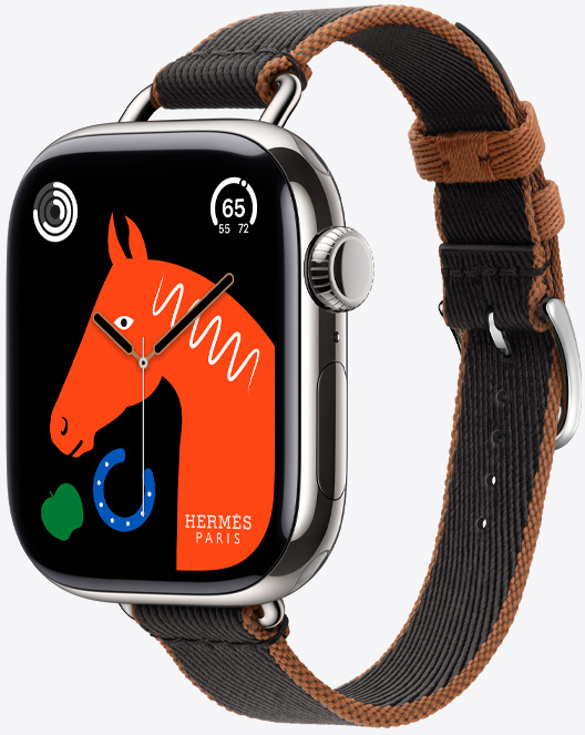 Angled view of the new Twill Jump Attelage Single Tour band in Noir/Gold (black with gold trim) with the 'Lucky Horse' watch face featuring an orange horse's head, a green apple, and a blue horseshoe.