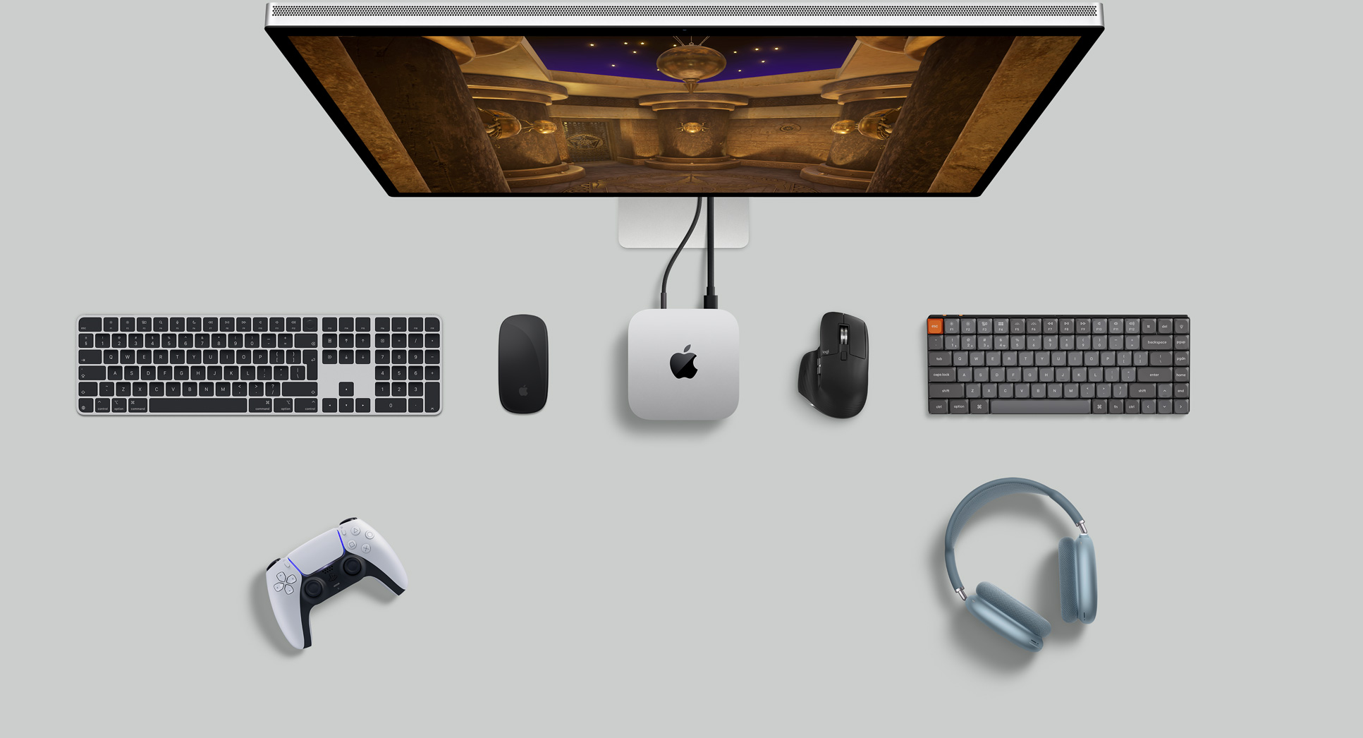 Vedere de sus a unui Mac mini argintiu într-o configurație de birou cu ecran, tastaturi wireless, mouse-uri wireless, un controler de jocuri și căști AirPods Max