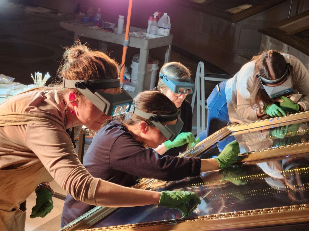 Color photograph showing Conservation staff members clean the casement holding the U.S. Constitution in the National Archives Rotunda 