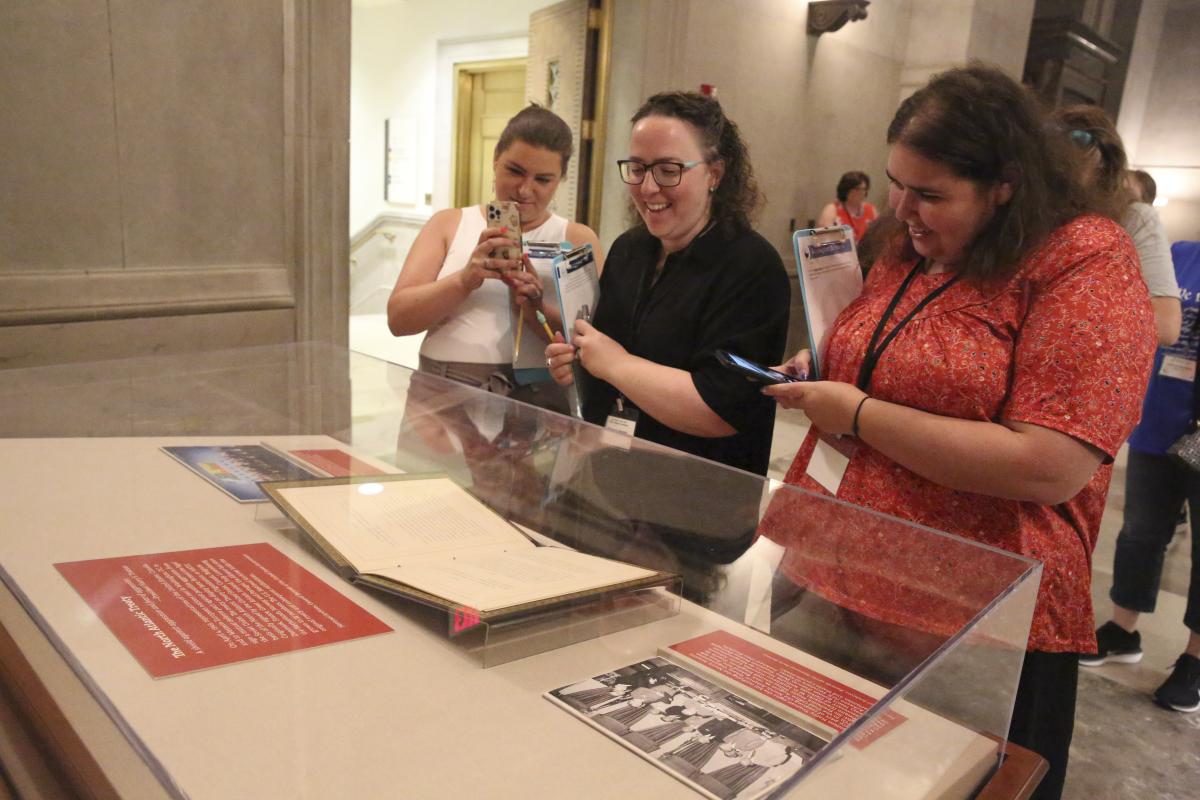 Color photograph of three White women looking at the treaty on display under a glass case and taking photos with their phones.