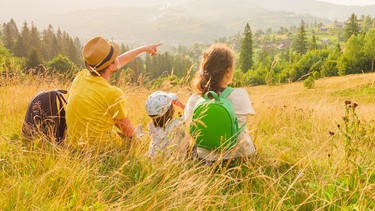 Vater, Mutter und kleines Kind ruhen sich im Gras von einer Wanderung aus.  | Bild: colourbox.com