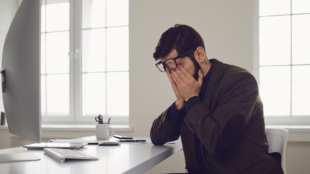 Mann sitzt in einem Büro und fasst sich an den Kopf. Hier erfahrt ihr, welche Formen von Perfektionismus es gibt, wann er krankhaft ist und wann er nützt.  | Bild: colourbox.com