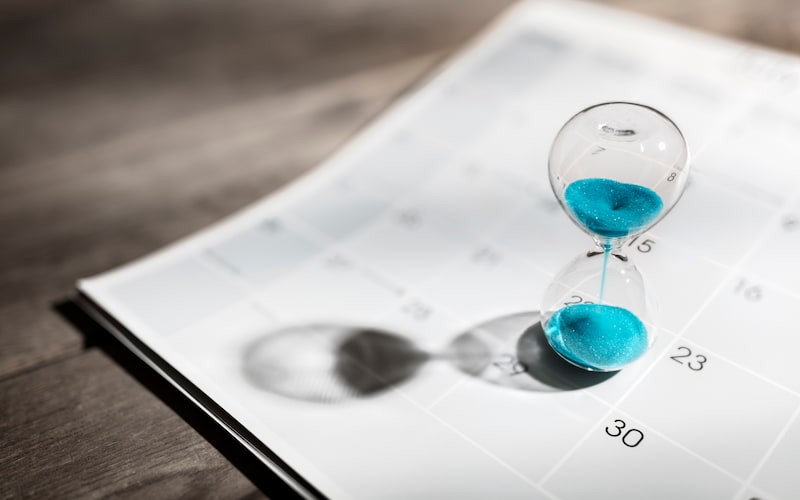 Hourglass with Blue Sand on top of Calendar