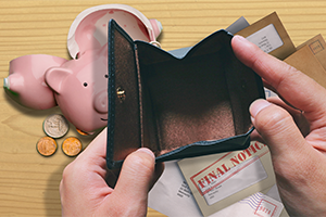 Picture of hands holding open an empty wallet with bills and a broken piggy bank