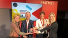 Freude beim Projektteam über die Preisverleihung: Das BR-Projekt "HbbTV Audiosync" wurde mit dem Connect! The Smart TV Award auf den Medientagen München 2021 in der Kategorie "Feels like Magic – Beste technologische Innovation" ausgezeichnet. Der Award zeichnet besondere Innovationen, Apps und Services rund um das vernetzte Fernsehen aus. Aus der Begründung der Jury: Barrierefreiheit zum Anhören: Mit der App „BR Audiodeskription” können Zuschauerinnen und Zuschauer am Smartphone eine für sie passende Tonspur am “Second Device” zum laufenden Fernsehbild auswählen. Das ist innovativ und inklusiv, denn es ermöglicht Menschen mit fehlendem oder stark eingeschränktem Sehvermögen per Kopfhörer ein gemeinschaftliches Fernseherlebnis zusammen mit Sehenden. Im Bild von links nach rechts: Kathleen Schröter (J2C) , Mitglied der Jury; Martin Hafner (BR), Ingrid Mitterhummer (BR), Kathrin Weinzierl (BR) | Bild: Kathleen Schröter/ Foto: Katharina Baer