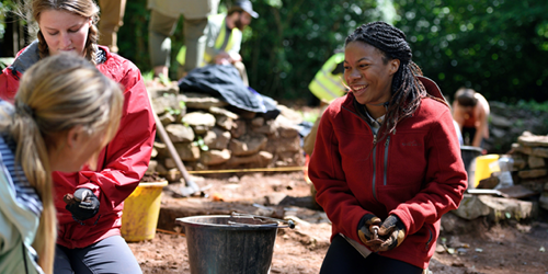 Student smiling while working on an archaeological dig site with other students.