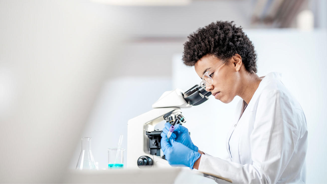 Female researcher writes on a sample vial while sitting by a microscope.