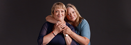 A woman with a blue shirt wraps her arms around another woman in a black shirt