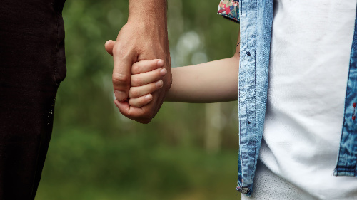 father holds his little son by the hand