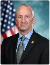 Troy A. Miller, CBP Senior Official Performing the Duties of the Commissioner seated in front of a blue background with a flag to the left.