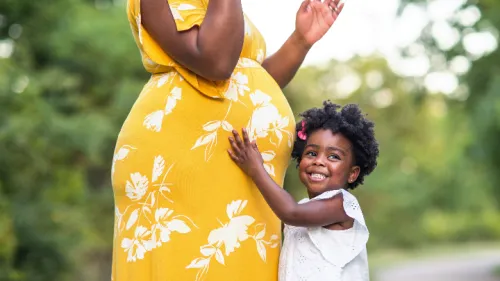 Little girl smiling holding her mother’s stomach who is pregnant.