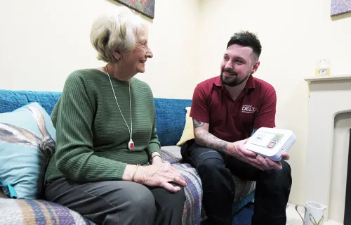 Delta Wellbeing worker talks to elderly care patient on sofa