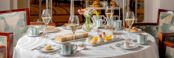 the foyer and reading room afternoon tea set up with sandwiches and pastries on table, scones with cream and jam in the background and champagne glasses filled