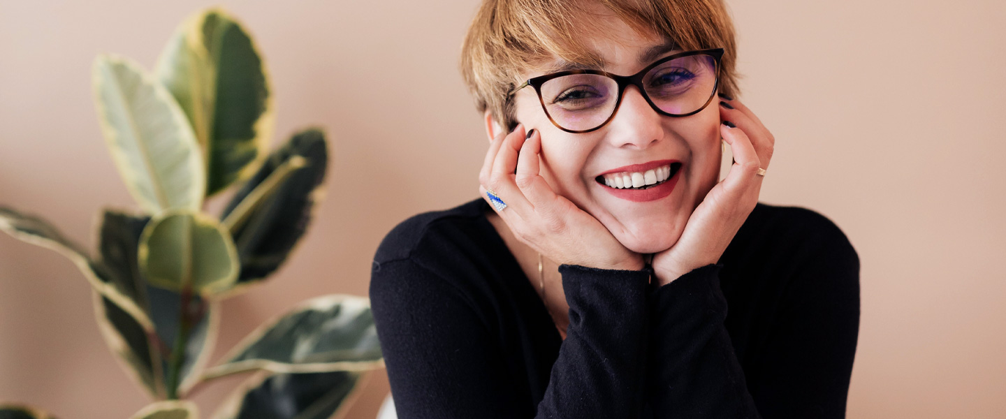 Frau mit Brille hat Hände im Gesicht und lächelt