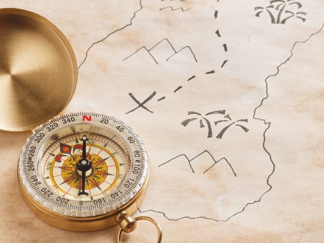 A golden compass lies on a treasure map with two sets of mountains and two sets of palm trees and a winding dotted path showing the way in piece about customer support in CX and strategies. 