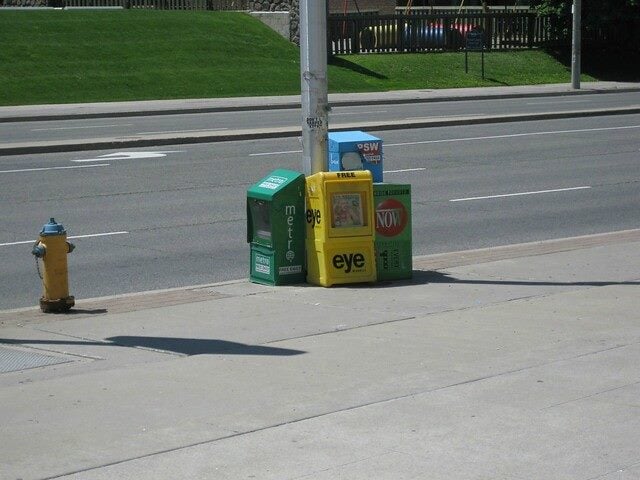 newspaper stands on a sidewalk near a road.