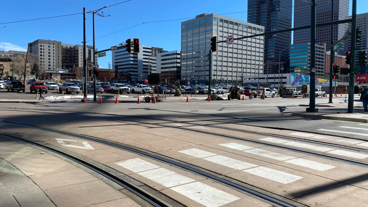 Train tracks run across a street with tall buildings in the background.