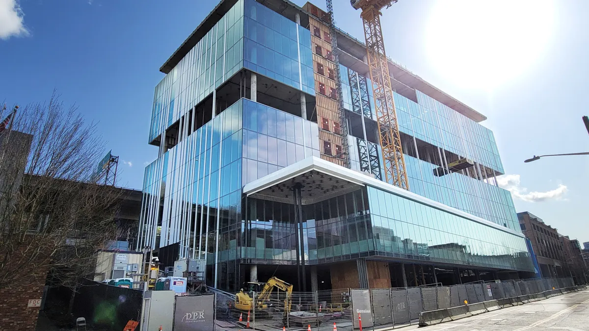 A yellow crane stands in front of a tall, shiny glass building that is mostly constructed.