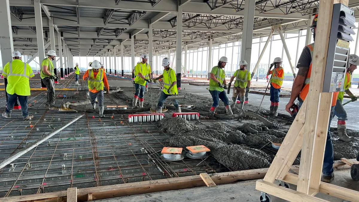 Several workers in safety gear work on a concrete pour inside a building under construction.