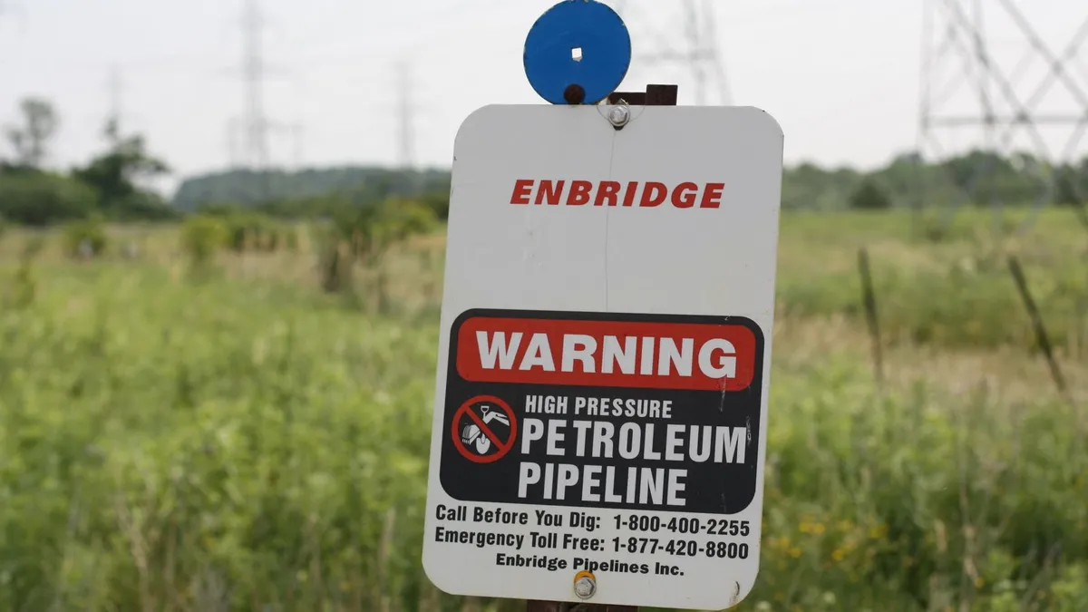 A white Enbridge buried pipeline marker for 'Line 9' stands in green grass.