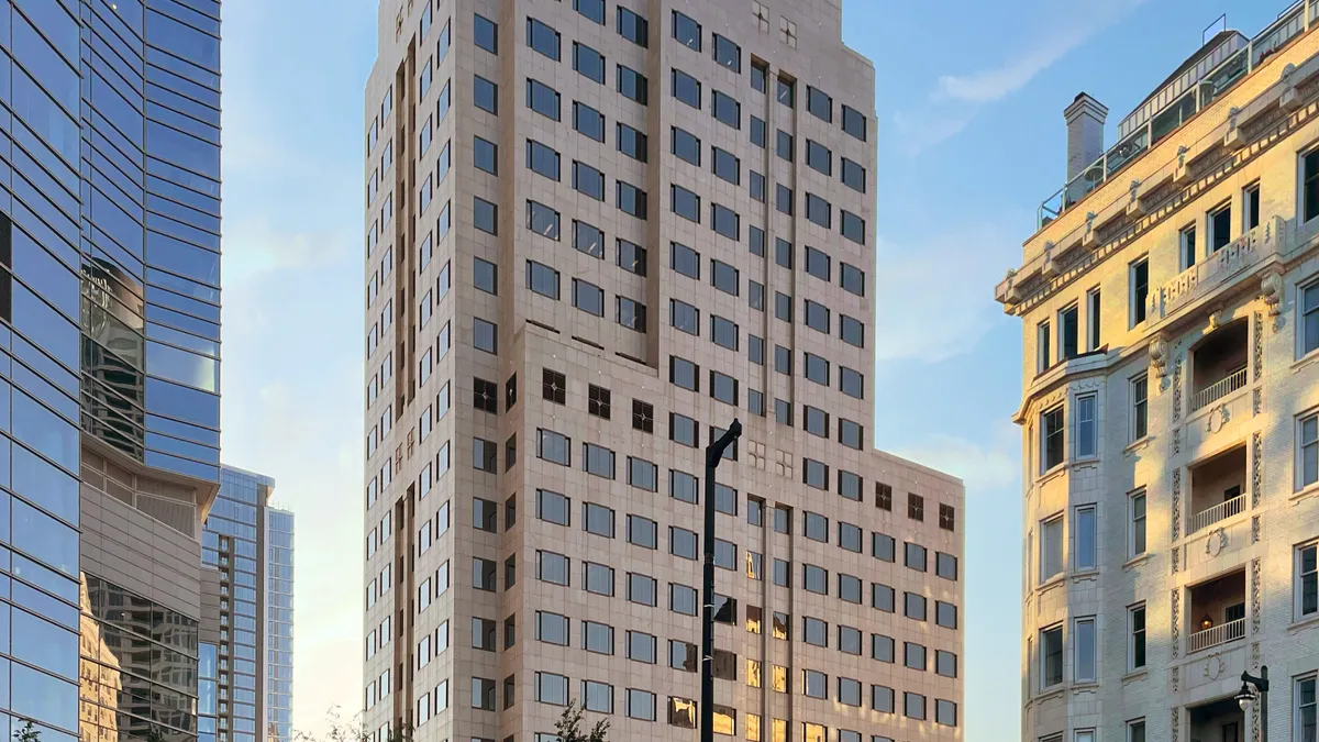 A brown stone building looms in a city background. It features partitioned windows, with brick and stone in-between.