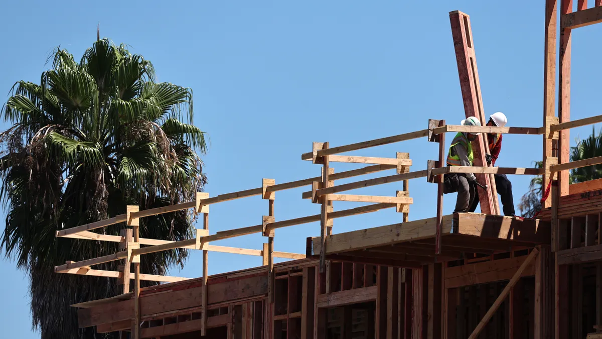 Two construction workers work together on a mixed-use apartment complex