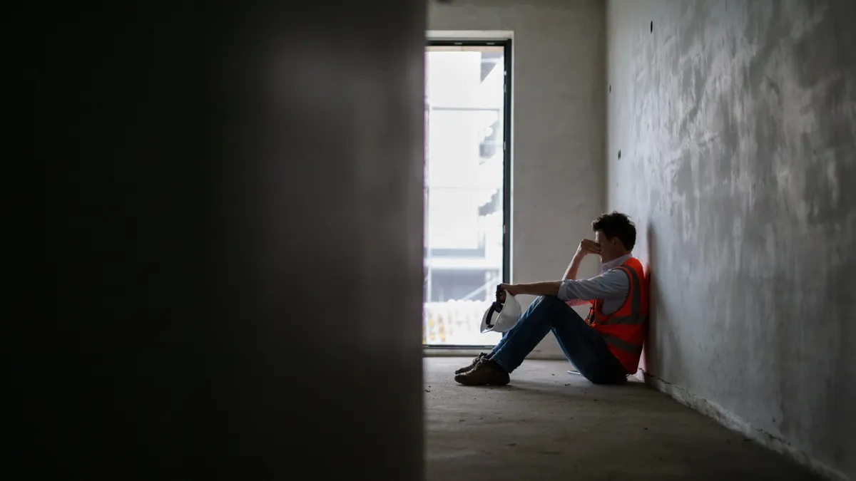 A construction worker sites on a jobsite, looking sad.