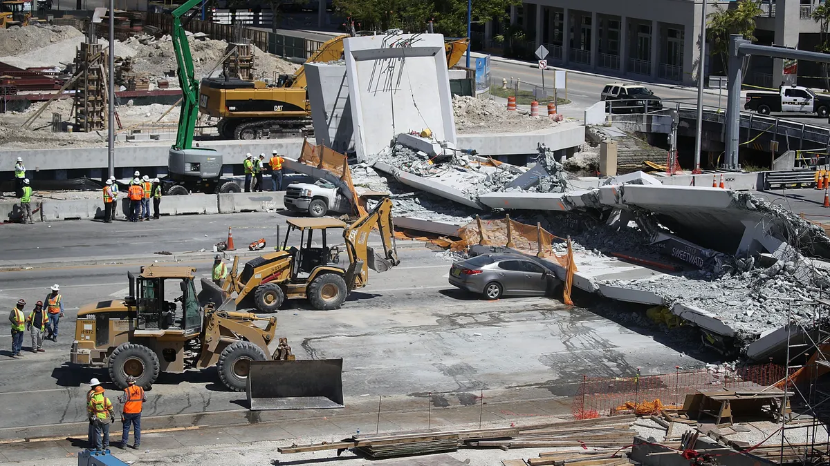 Construction crews and machinery surround a collapsed bridge over a road.