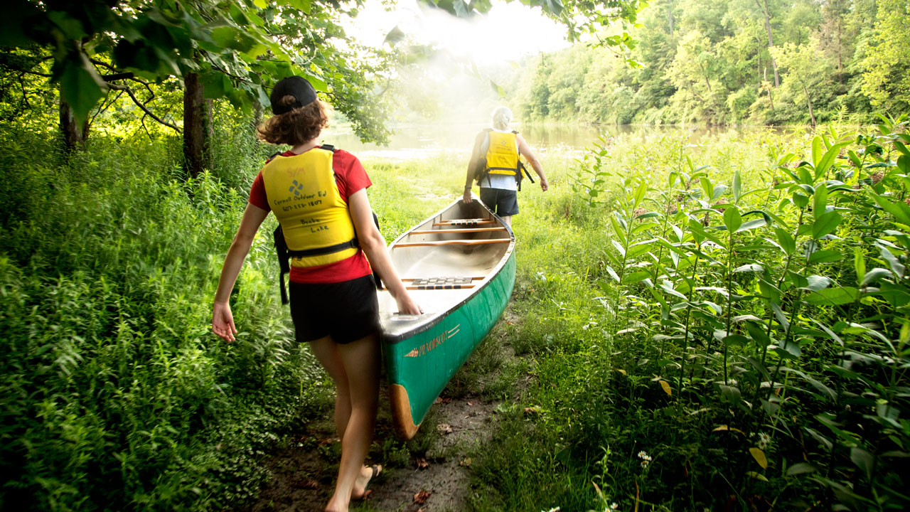 Two people carrying a canoe to Beebe Lake.