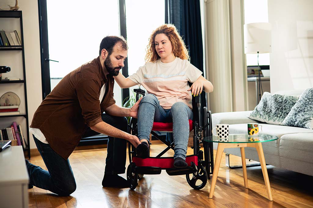 A man helping his girlfriend in her wheelchair with her leg.