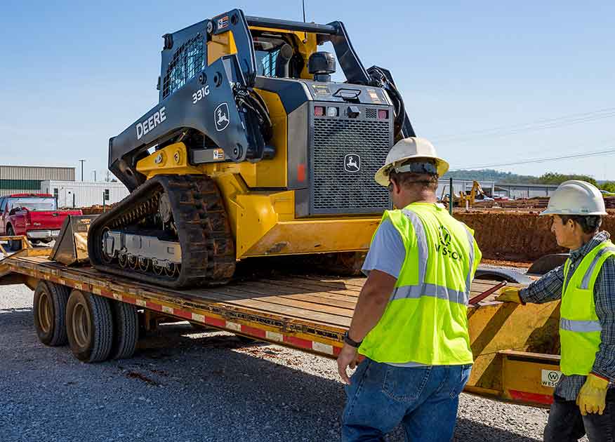 Two men standing next to a trailer with a a John Deere 331G on it