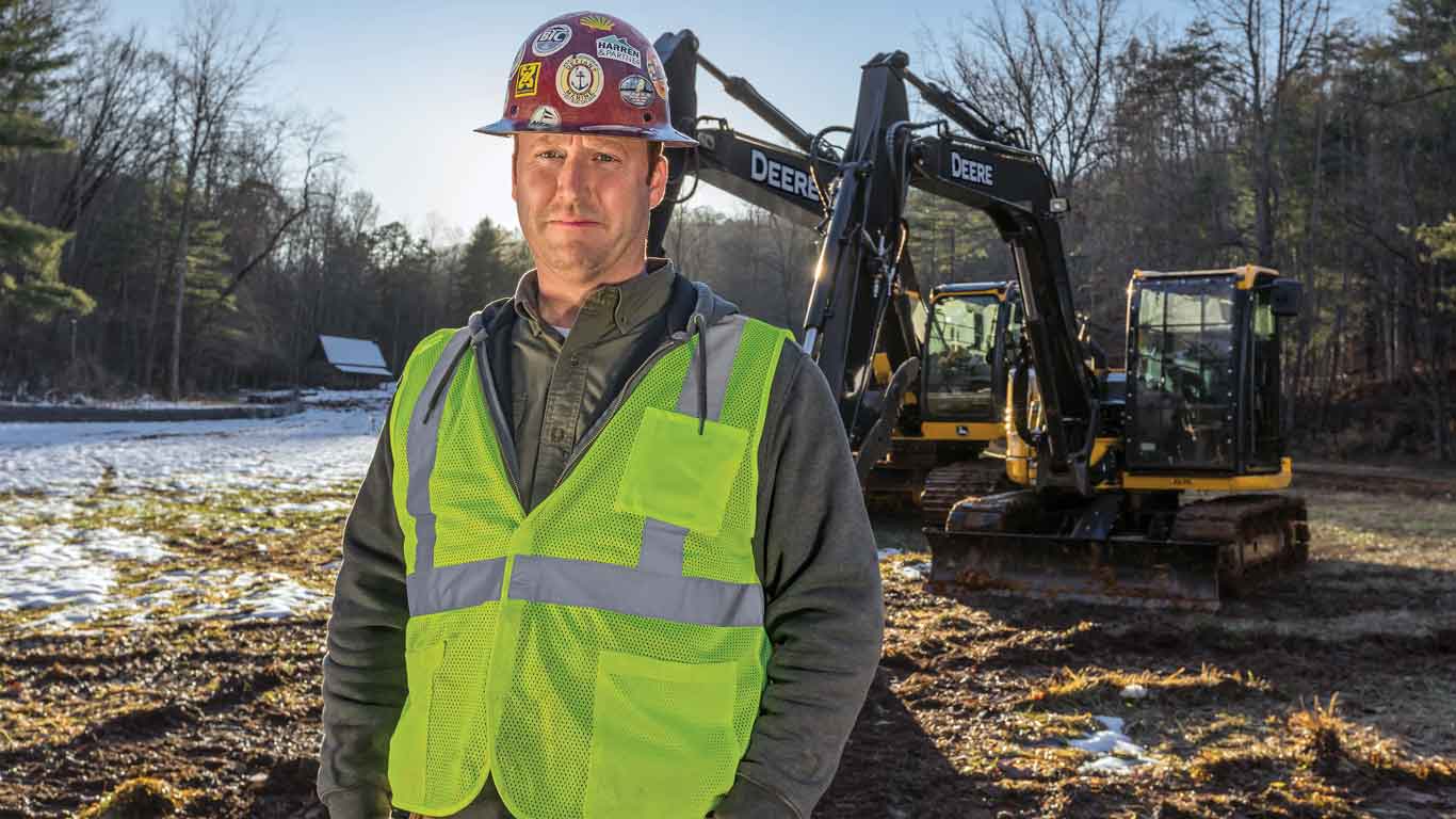 Man in hard hat and reflective vest with John Deere Construction equipment in the background