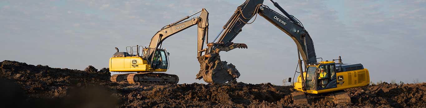 Two large yellow John Deere excavators digging a trench in a brown field