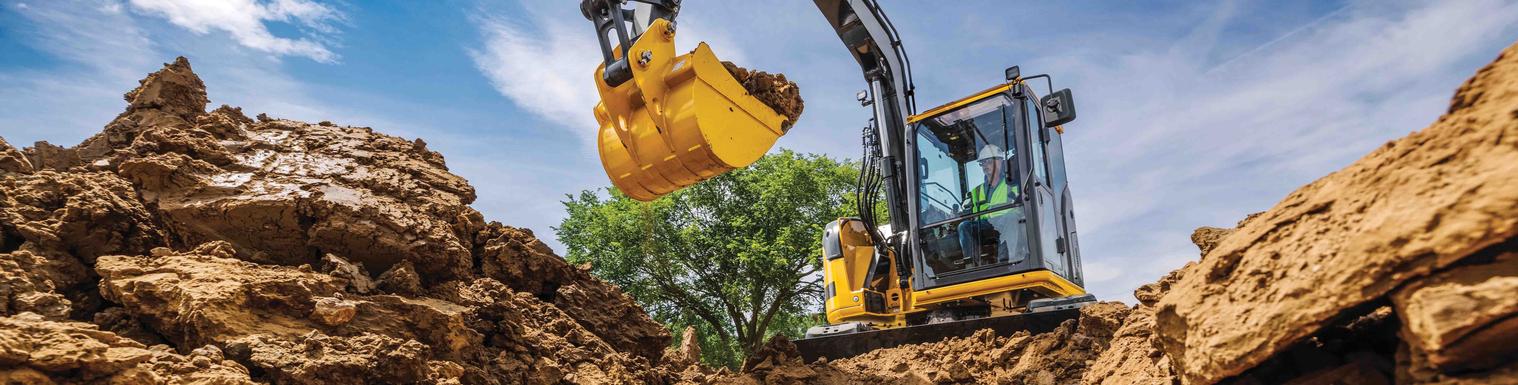 John Deere Excavator works on digging a large hole with blue sky in the background