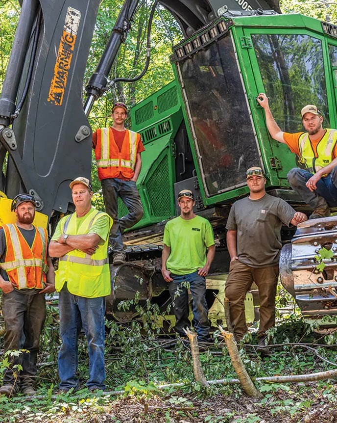 Standing within the Michigan woods, Max Tervo, Doug Anderson, Ladd Anderson, Nash Anderson, Eli Larson, and Dane Anderson, all of Doug Anderson Logging, stand beside an 853M Tracked Feller Buncher.