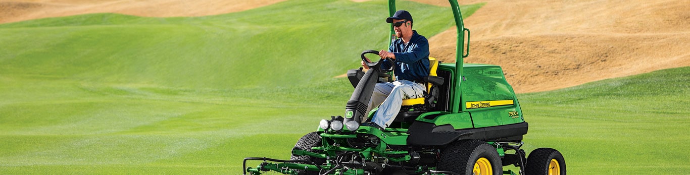 Man mowing a golf green with a riding John Deere mower.