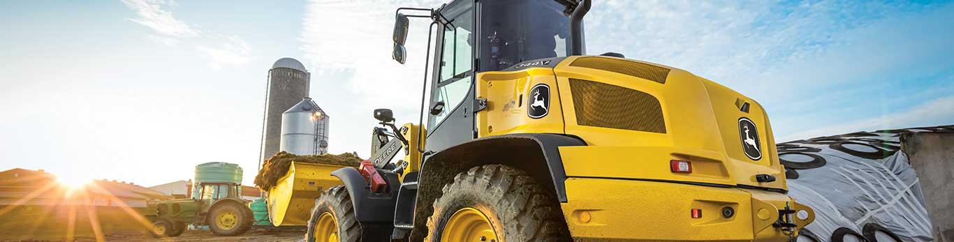 Compact Loader lifts a load of dirt while facing the sun.